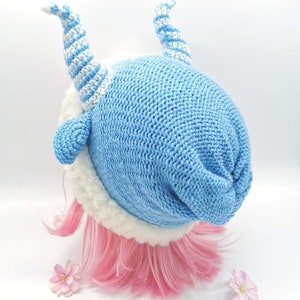 May include: A blue knitted hat with white stripes and a white fur trim. The hat has two white and blue striped horns on top.