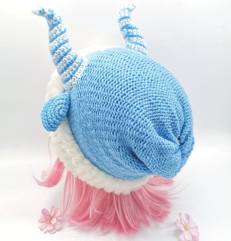 May include: A blue knitted hat with white stripes and a white fur trim. The hat has two white and blue striped horns on top.