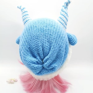 May include: A blue knitted hat with white striped horns. The hat has a white fur trim around the bottom edge.