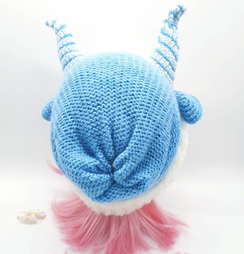 May include: A blue knitted hat with white striped horns. The hat has a white fur trim around the bottom edge.