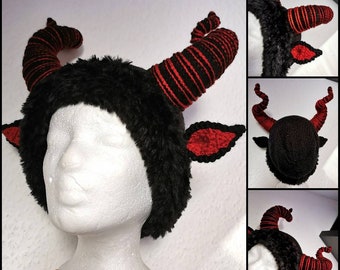 May include: A black and red horned headpiece with a furry texture. The horns are striped with red and black yarn. The ears are red with black trim. The headpiece is displayed on a white mannequin head.