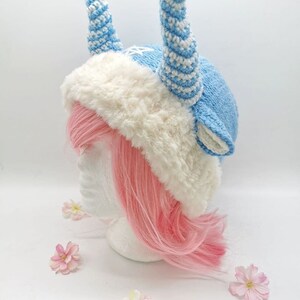 May include: A blue and white crocheted hat with horns, a white faux fur brim, and a pink wig on a white mannequin head.