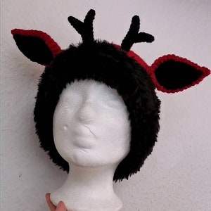 Puede incluir: Un gorro de cuernos de reno negro y rojo con detalles de piel sint&eacute;tica y ganchillo. El gorro presenta una base de piel sint&eacute;tica negra con ribete rojo y orejas rojas y negras a juego. Los cuernos son negros.