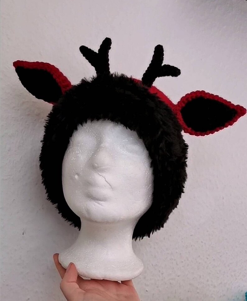 Puede incluir: Un gorro de cuernos de reno negro y rojo con detalles de piel sint&eacute;tica y ganchillo. El gorro presenta una base de piel sint&eacute;tica negra con ribete rojo y orejas rojas y negras a juego. Los cuernos son negros.