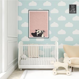 Puede incluir: Un gato blanco y negro mirando hacia arriba a un tri&aacute;ngulo rosa sobre un fondo estampado rosa y blanco. La imagen est&aacute; enmarcada y colgada en una pared azul claro con recortes de nubes blancas. Una cuna blanca y un caballo de balanc&iacute;n de madera est&aacute;n en primer plano.