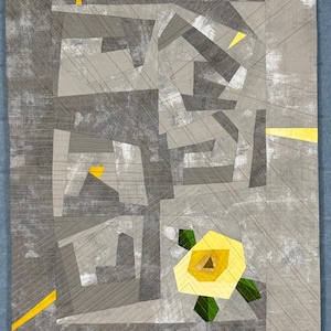 Könnte beinhalten: Abstrakte geometrische Steppdecke in Grautönen mit gelben und grünen Akzenten. Das Design zeigt eine kantige Formgebung und eine stilisierte gelbe Blume unten. Maschinell gesteppt mit texturierter Oberfläche.