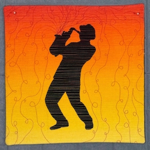 Könnte beinhalten: Ein quadratisches, gewebtes Wandbehang mit einer schwarzen Silhouette eines Saxophonspielers. Der Hintergrund wechselt von Gelb zu Orange, mit wirbelnden Linien. Das Stück ist mit einem gewebten Rand versehen und mit zwei Stiften befestigt.