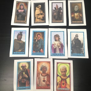 以下が含まれることがあります： 10枚のカラフルなカードのセットで、各カードに異なるキャラクターとテキストが描かれています。カードは白い紙に印刷されており、青い縁取りがされています。キャラクターは宗教的なスタイルで描かれており、後光と金色のアクセントが施されています。カードのテキストには、「私は正義の支配者です」、「私を愚か者扱いしないでください」、「もしかしたら、正気の一筋の光があったのかもしれません」などのフレーズが含まれています。