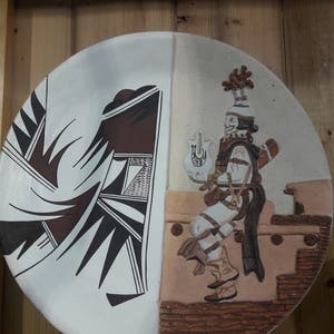 May include: A white ceramic plate with a brown and black geometric design on the left side and a brown and white relief sculpture of a person in traditional clothing on the right side.