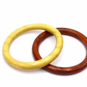 Könnte beinhalten: Zwei Holzringe, einer hellgelb und einer dunkelbraun, sind ineinander verschlungen. Die Ringe sind glatt und haben eine natürliche Holzoptik.