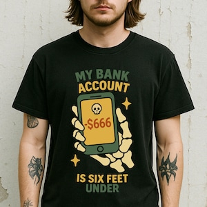 May include: Black t-shirt with a graphic of a skeleton hand holding a smartphone. The phone screen displays a skull and the text "-$666". The text on the shirt reads "My bank account is six feet under."