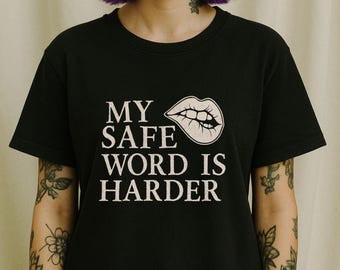 Op de afbeelding: Zwart T-shirt met witte tekst die "My safe word is harder" luidt en een zwart-witte illustratie van een mond met tanden.