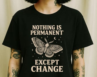 May include: Black t-shirt with the text "NOTHING IS PERMANENT EXCEPT CHANGE" and a moth illustration. The moth is detailed with eye-like markings and surrounded by stars and a crescent moon. The text and moth are in a light beige color.