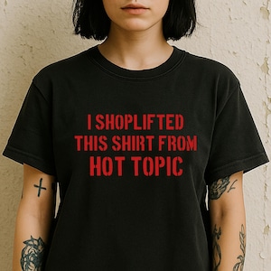 May include: Black crew neck t-shirt with the red text "I SHOPLIFTED THIS SHIRT FROM HOT TOPIC" printed across the front. The shirt has short sleeves and a slightly faded appearance.