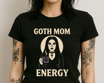 Könnte beinhalten: Schwarzes T-Shirt mit dem weißen Schriftzug "GOTH MOM ENERGY". Die Grafik zeigt eine Frau mit langen schwarzen Haaren, die eine lila Tasse mit einem Pentagramm hält. Sie trägt ein schwarzes Halsband mit Kreuzanhänger.