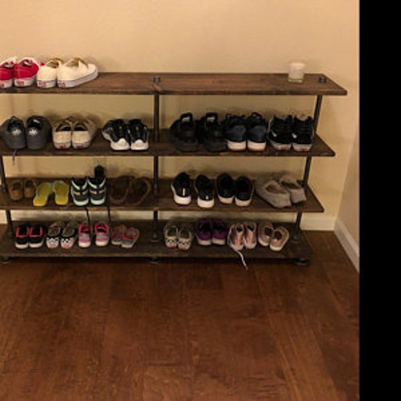 May include: A four-tier wooden shoe rack with black metal pipes for support. The rack is filled with various shoes, including trainers, sandals, and slippers.