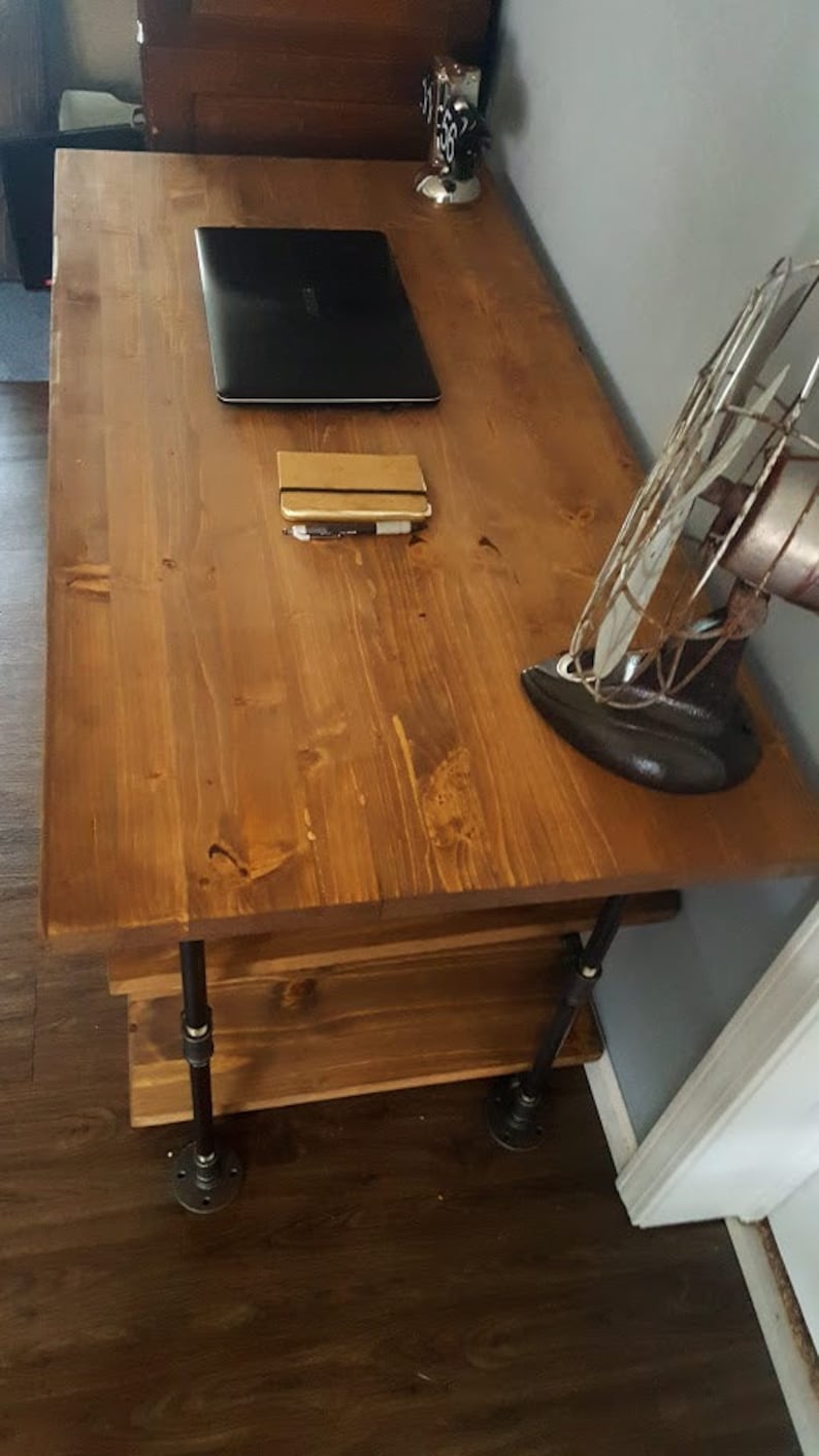 K&ouml;nnte beinhalten: Ein Holzschreibtisch mit dunkelbrauner Oberfl&auml;che und schwarzen Metallrohrbeinen. Ein Laptop, ein Notizbuch und ein Vintage-Ventilator stehen auf dem Schreibtisch.