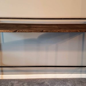 May include: A rustic wooden bar table with black metal pipe legs and a top rail. The table has a dark brown stain and is made of reclaimed wood.