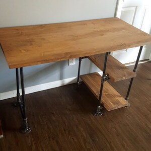 K&ouml;nnte beinhalten: Ein Holzschreibtisch mit einer braunen Tischplatte und schwarzen Metallbeinen aus Rohren. Der Schreibtisch hat zwei Regale aus Holz und Metallrohren.