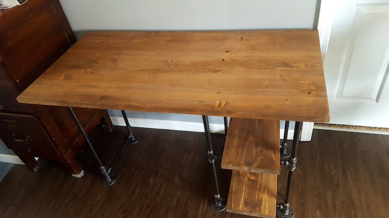 K&ouml;nnte beinhalten: Ein Holzschreibtisch mit einer braun gebeizten Platte und schwarzen Metallrohrbeinen. Der Schreibtisch hat zwei Regale unter der Platte.