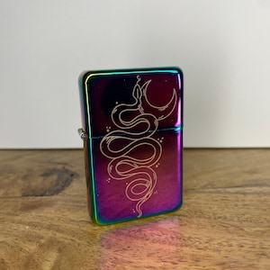 Pu&ograve; includere: Un accendino iridiscente arcobaleno con un designo inciso a laser di un serpente avvolto attorno a una luna crescente.
