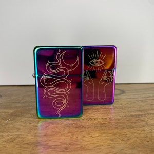 Pu&ograve; includere: Due accendini in metallo iridescente con disegni incisi. Un accendino presenta un serpente con una luna crescente, l'altro presenta due mani che tengono un occhio.