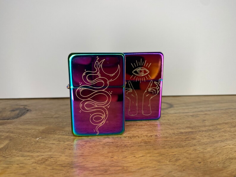 Pu&ograve; includere: Due accendini in metallo iridescente con disegni incisi. Un accendino presenta un serpente con una luna crescente, l'altro presenta due mani che tengono un occhio.