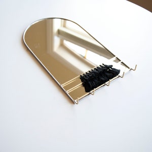 May include: A silver arched mirror with a black tassel hanging from the bottom. The mirror has three hooks on the bottom.