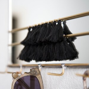 May include: A gold metal rack with black tassel trim hanging from the top. Sunglasses are hanging from the bottom of the rack.