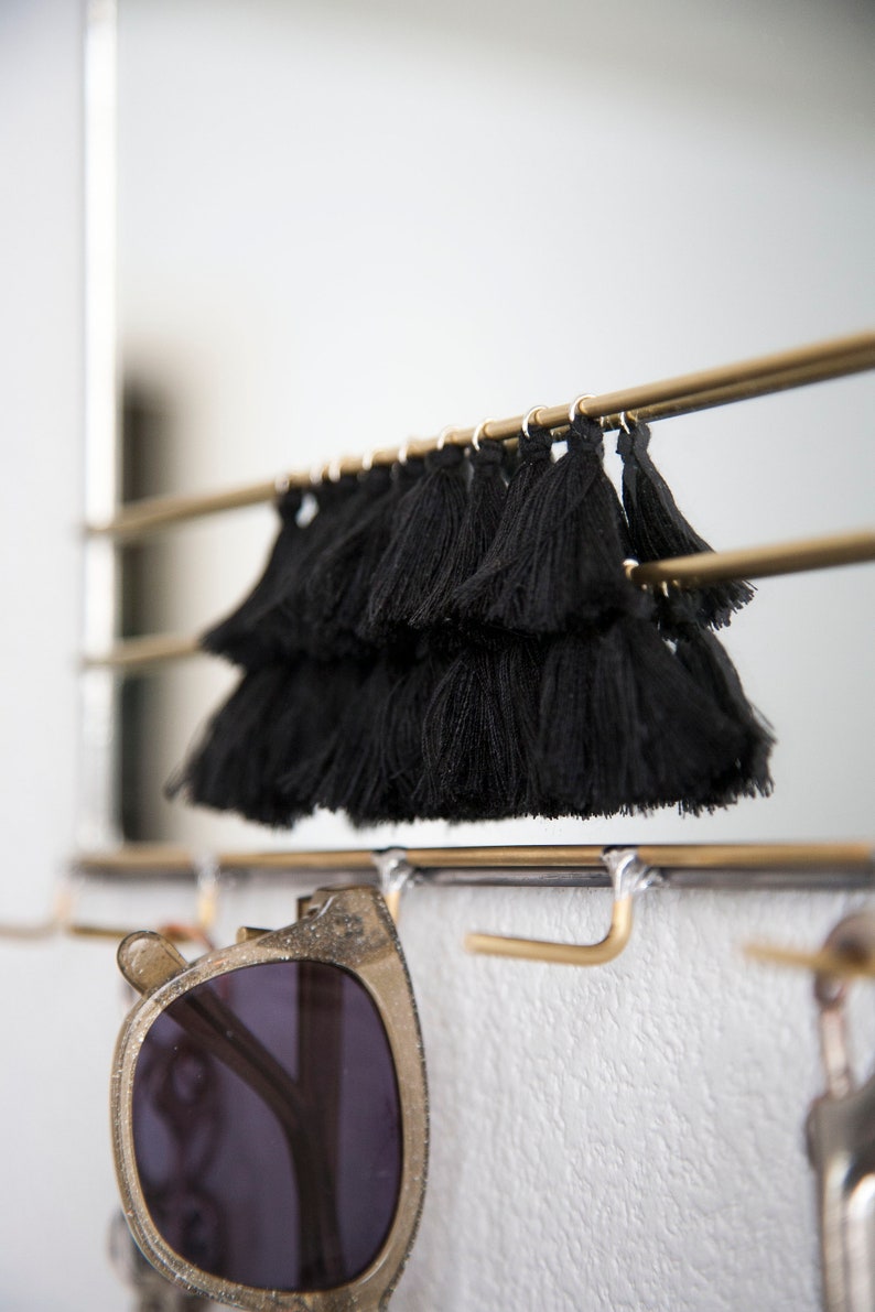 May include: A gold metal rack with black tassel trim hanging from the top. Sunglasses are hanging from the bottom of the rack.
