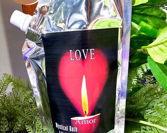 May include: A silver pouch of Mystical Bath with a black label featuring a red heart with a candle flame and the word "LOVE". The word "Amor" is below the heart. The pouch has a white spout.