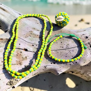 May include: A long necklace, a matching bracelet with a green adjustable cord, and a spherical bead ornament, all crafted from alternating yellow and green seed beads. The spherical ornament features a white cowrie shell at its center.