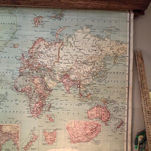 May include: An antique world map, featuring continents in shades of pink and green, is mounted on a wooden frame. The map displays detailed geographical features and is likely a vintage educational or decorative item.