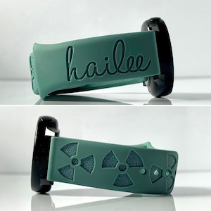 May include: A green smartwatch band with the name "hailee" engraved on it. The band is also shown with a pattern of three black radiation symbols.