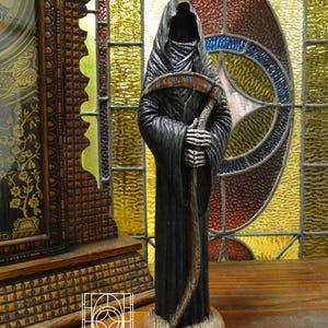 May include: A grim reaper figurine wearing a long, textured black hooded robe. The figure has skeletal hands holding a scythe with a curved, weathered blade and a wooden-textured handle. It stands on a circular base with the text JPerryKeepsakes.