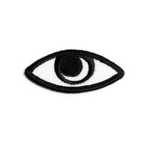 May include: Embroidered eye patch in black and white. The eye is a stylized design with a black pupil and iris, surrounded by a white eye and a black border. The patch is likely for clothing or accessories.