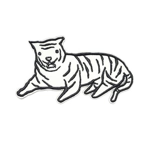 Puede incluir: Parche bordado en blanco y negro con un tigre de dibujos animados en posición relajada. El tigre tiene rayas y contornos negros, con una expresión sonriente. El parche es probablemente para ropa o accesorios.