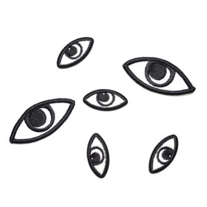 May include: Six black embroidered eye patches with white outlines. The eyes are all different sizes and shapes.