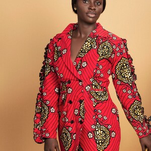 May include: A red dress with a black and gold floral pattern. The dress has a long sleeve with ruffles on the shoulders and a double breasted closure.
