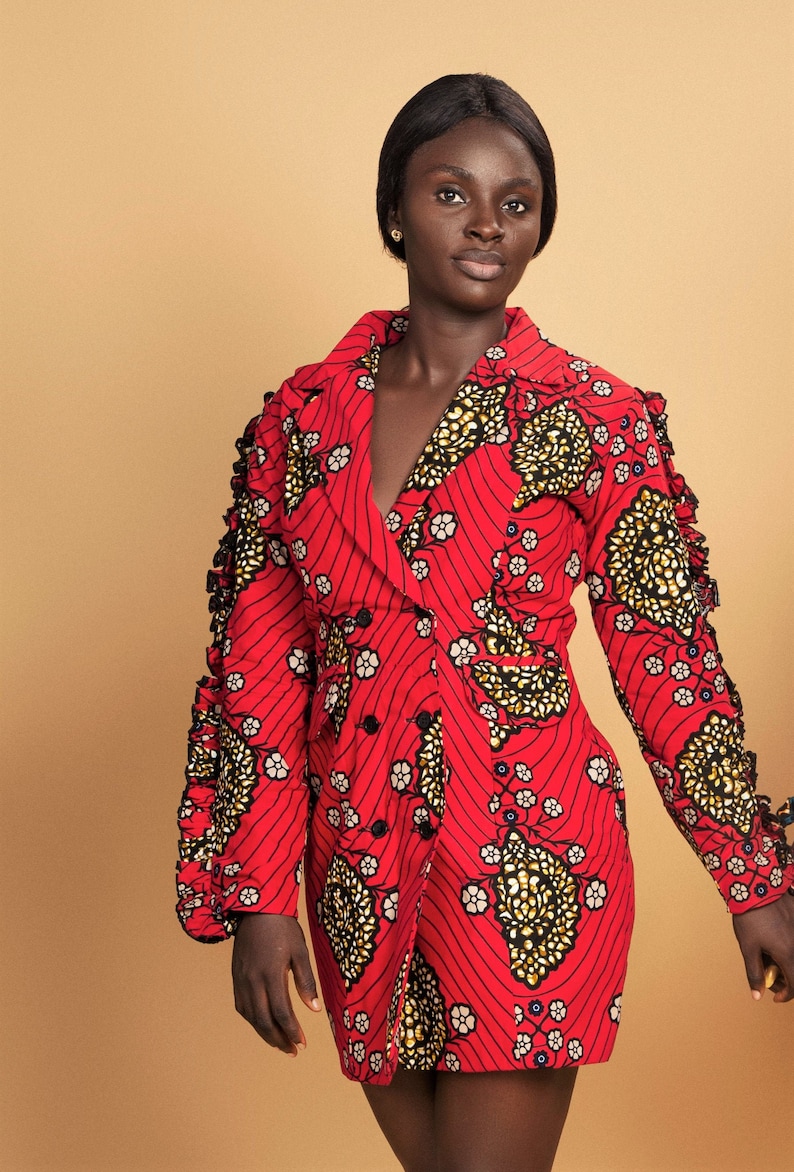 May include: A red dress with a black and gold floral pattern. The dress has a long sleeve with ruffles on the shoulders and a double breasted closure.