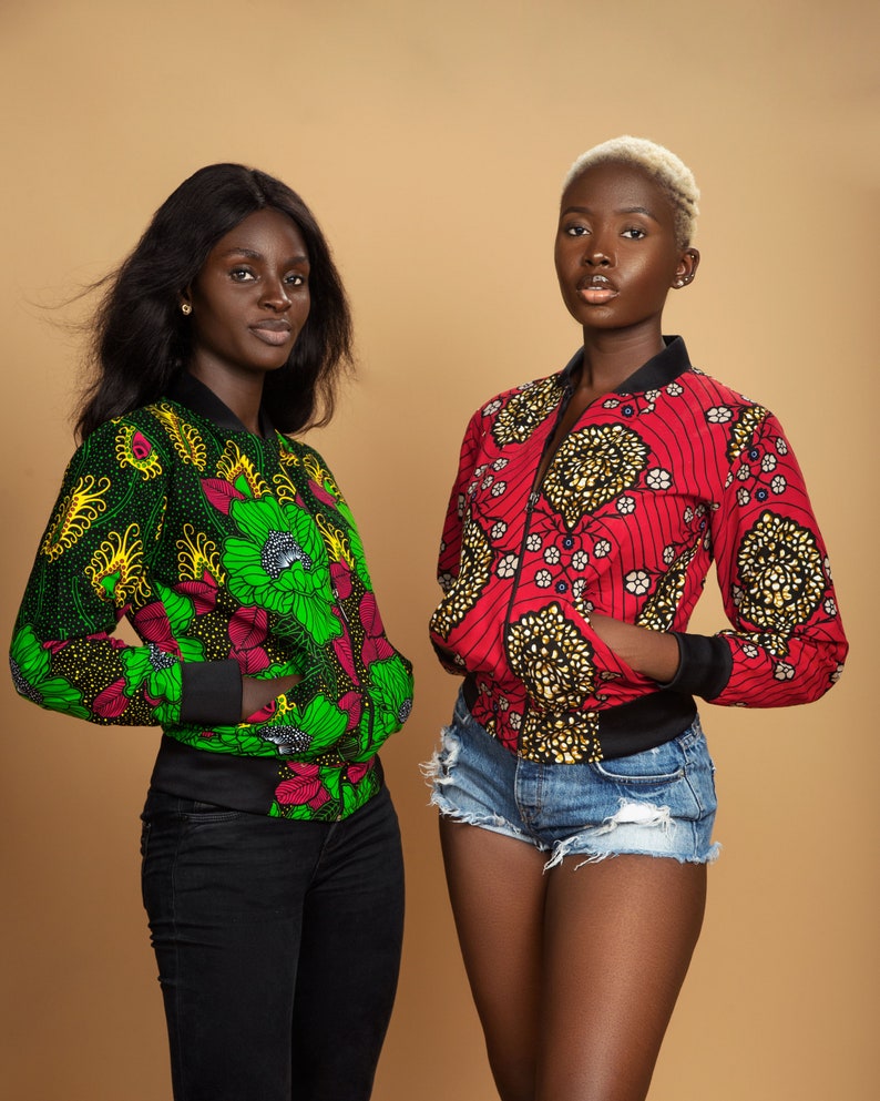 Puede incluir: Dos mujeres con chaquetas bomber de estampado colorido. Una mujer lleva una chaqueta verde y negra y la otra una chaqueta roja y negra. Ambas mujeres llevan pantalones negros y tienen la piel oscura.