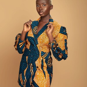 May include: A woman wearing a short, double-breasted blazer with a colorful geometric pattern in shades of blue, yellow, and orange. The blazer has a ruffled detail on the sleeves.