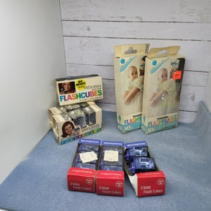 May include: A collection of vintage flash cubes in blue and white packaging. The packaging features the brand name "Sylvania" and the text "Flashcubes" and "Flashbulbs". There are three packs of flash cubes in blue and white packaging labeled "Westinghouse" with the text "3 blue Flash Cubes".