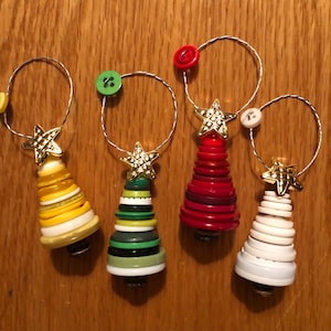 May include: Four handmade Christmas tree ornaments. Each tree is crafted from stacked buttons in shades of yellow, green, red, and white. A gold star tops each tree, and a button and wire loop are at the top for hanging.
