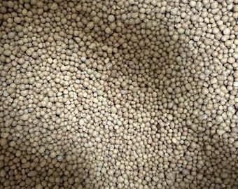 May include: Close-up of a pile of small, round, light brown pellets. The pellets are densely packed together, creating a textured surface. The color is consistent throughout, with slight variations in tone.