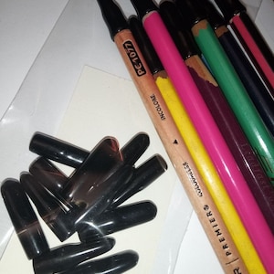 May include: A close-up of a set of colored pencils with black caps. The pencils are arranged in a row and are labeled with the brand name "COLOR PREMIER" and the text "INCOLORE" and "PC-1077".