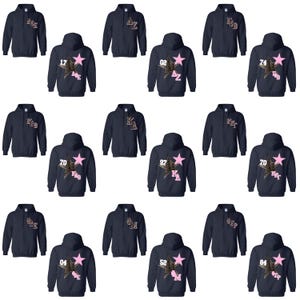 May include: Navy blue hooded sweatshirts with various designs. Each sweatshirt features a pink star with a leopard print pattern and a unique combination of letters and numbers. The sweatshirts are displayed on a white background.