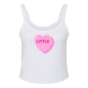 K&ouml;nnte beinhalten: Ein wei&szlig;es Tanktop mit einem rosafarbenen herzf&ouml;rmigen Bonbon, auf dem das Wort "LITTLE" steht.