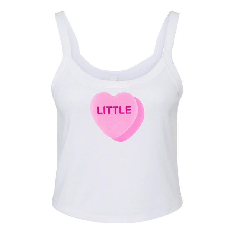 K&ouml;nnte beinhalten: Ein wei&szlig;es Tanktop mit einem rosafarbenen herzf&ouml;rmigen Bonbon, auf dem das Wort "LITTLE" steht.