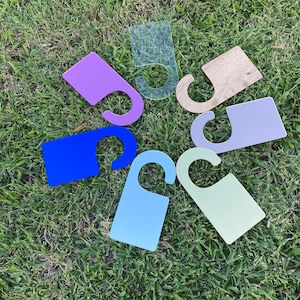 May include: A set of eight door hangers in various colours, including blue, purple, light blue, green, and brown. The hangers are made of a sturdy material and have a simple, modern design.
